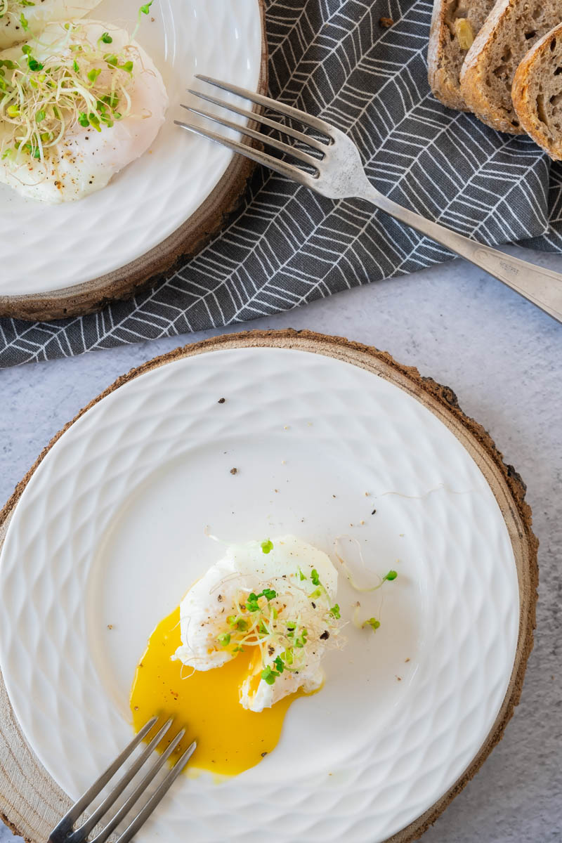 Poached eggs on plate with watercress on top, oozing egg yolk.