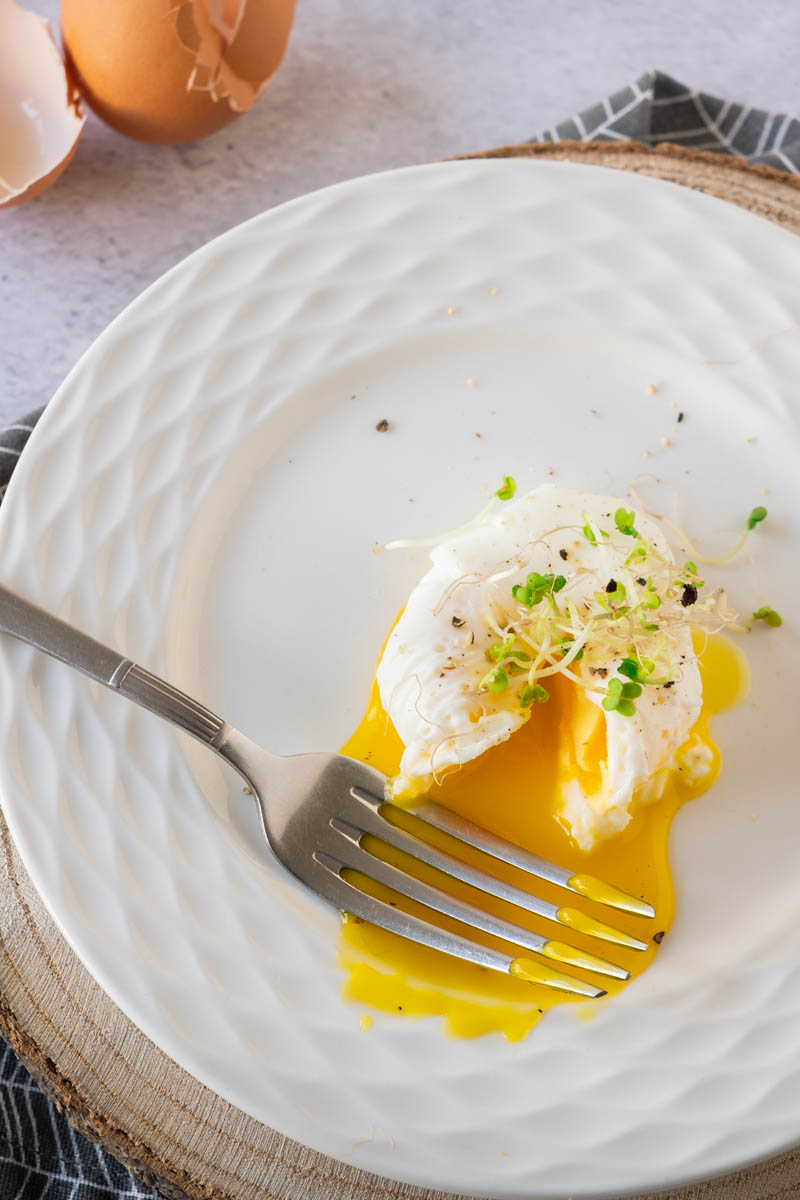 Poached eggs on plate with watercress on top, oozing egg yolk.