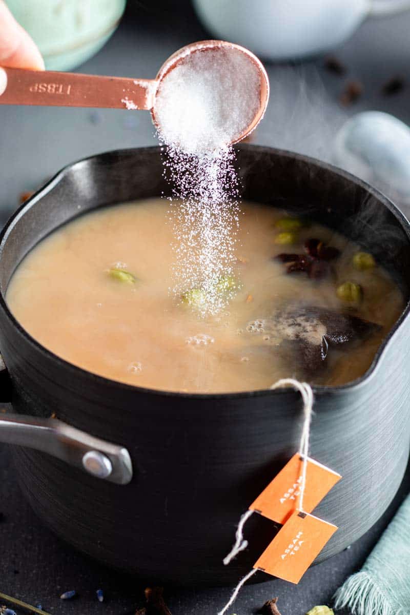 adding sugar to chai tea in pot