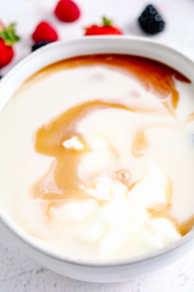 Full-fat yogurt whisked together with oat milk, and vanilla extract in a mixing bowl.