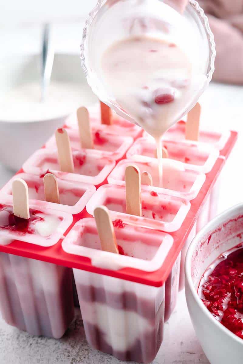 spooning vanilla yogurt into popsicle molds