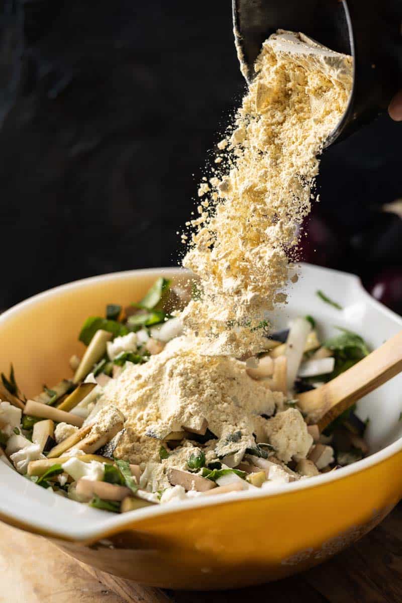 pouring chickpea flour into bowl of mixed vegetables