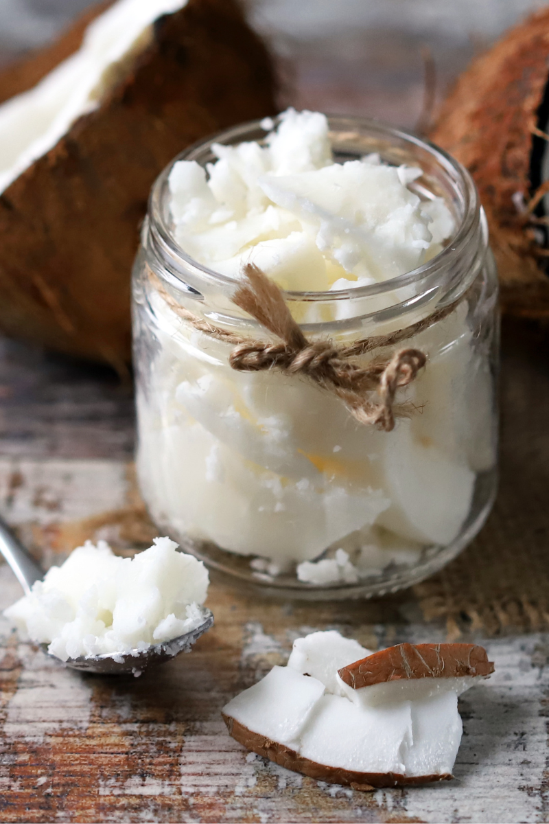Coconut oil in a jar, surrounded by coconuts.
