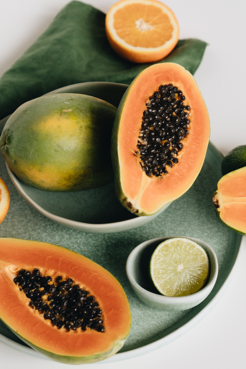 whole and cut papayas, in bowls, on on a white background.