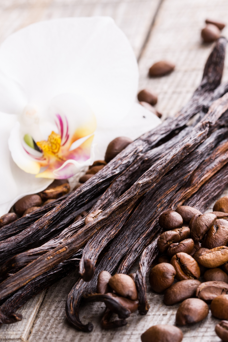 vanilla bean pods and coffee beans on a light wood surface.