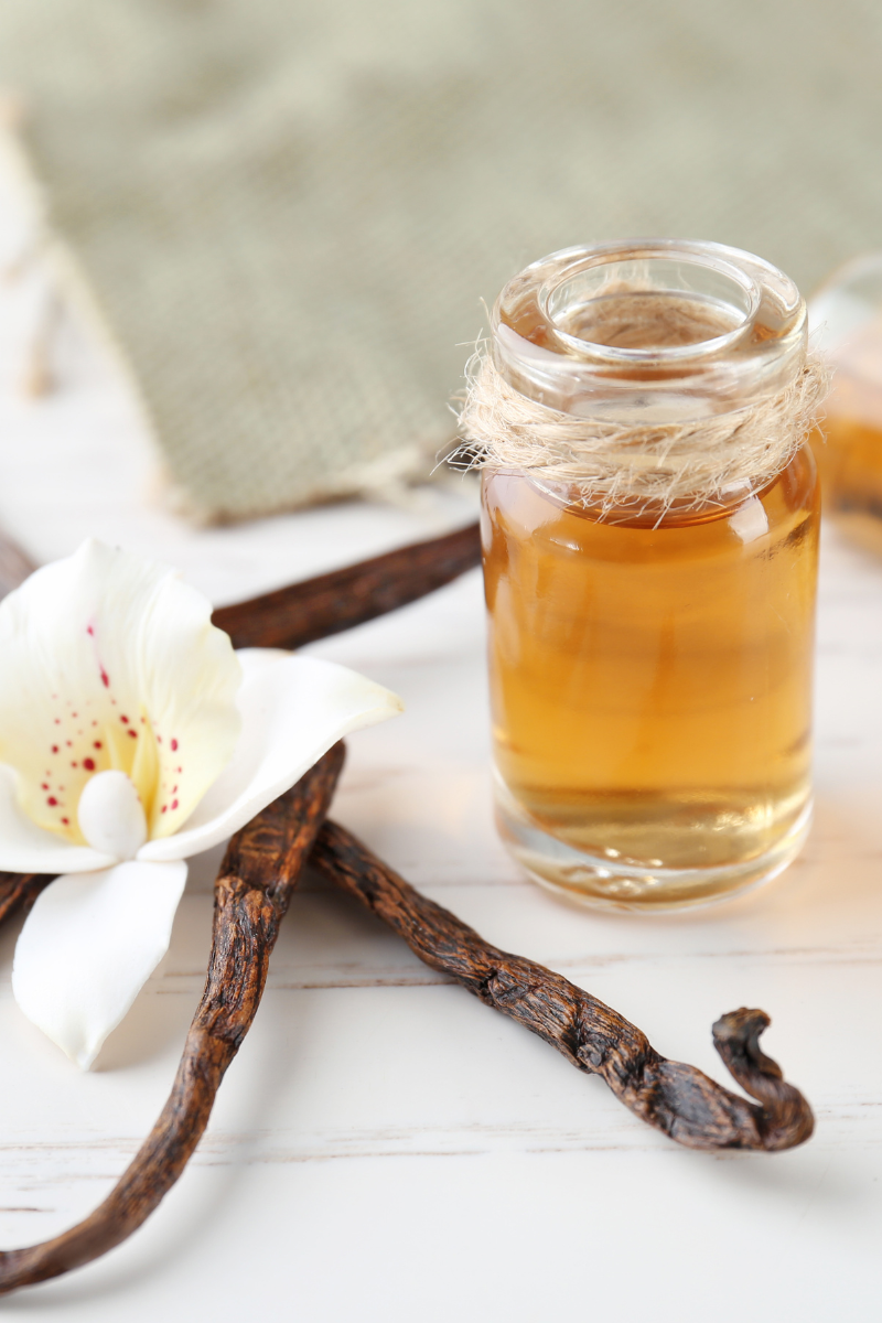 vanilla bean pods and vanilla extract on a light wood surface.
