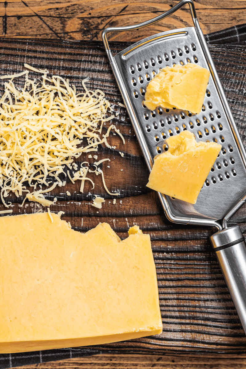 Cheddar cheese and hand grater on a wooden background.