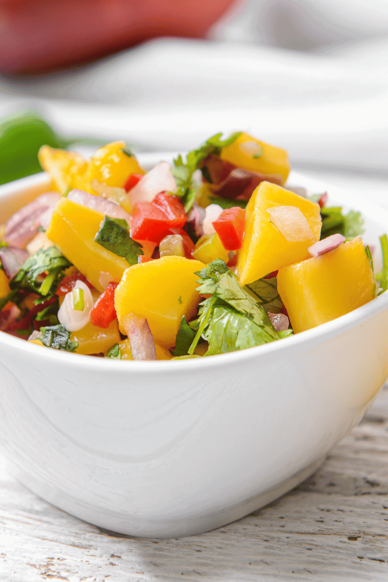 Mango salad in a white bowl on a wooden surface.