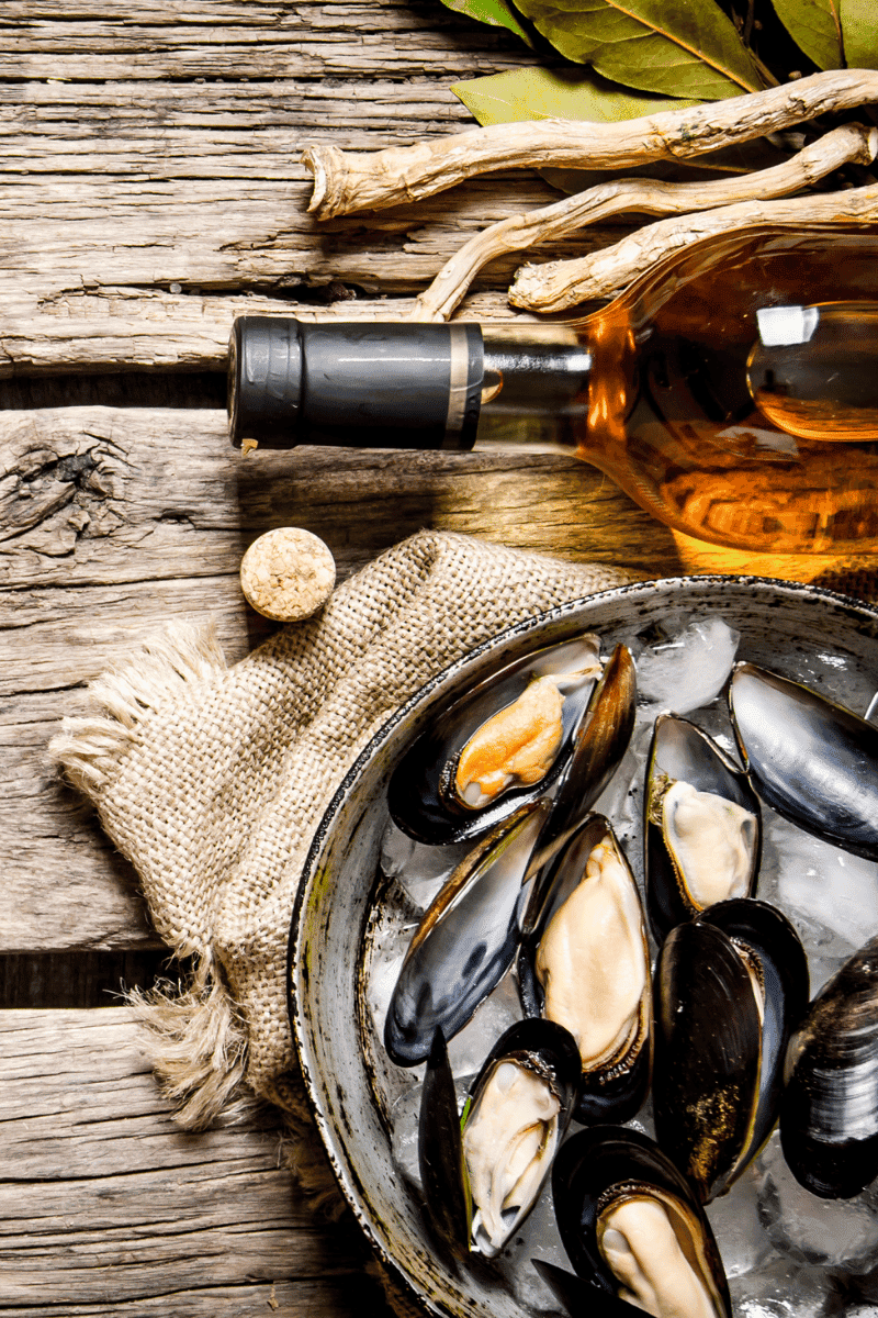 Clams on a plate next to a bottle of wine.