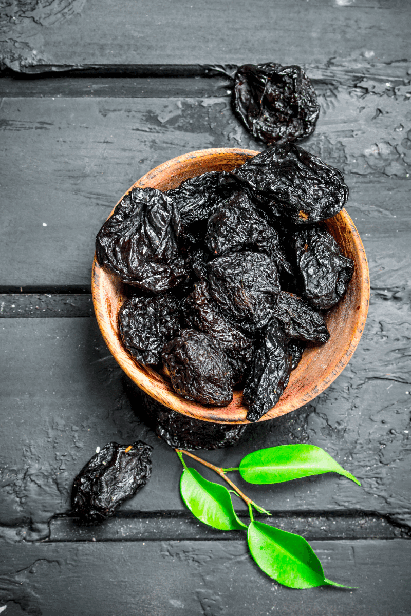 Prunes in a bowl on a dark plaster surface.