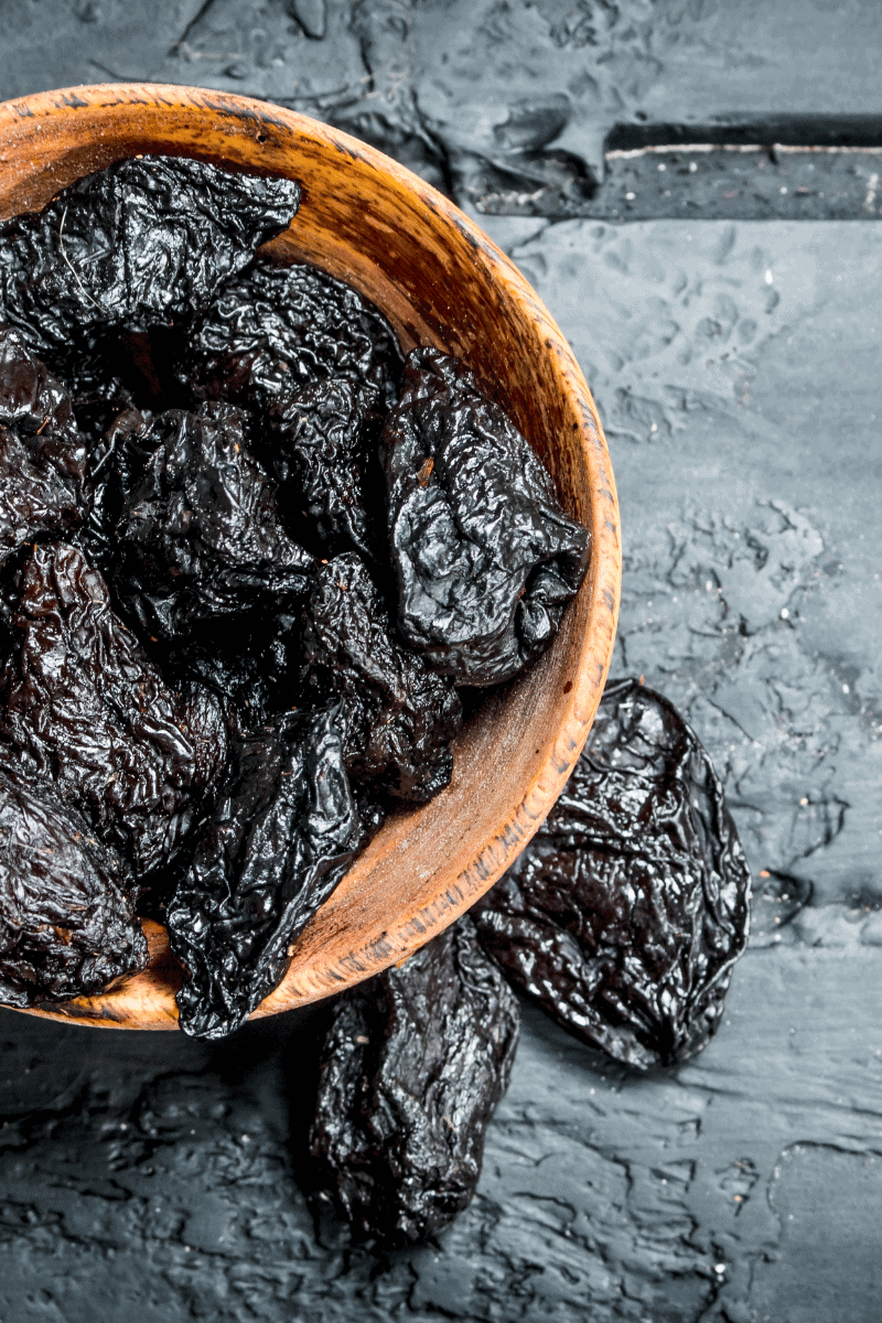 Prunes in a bowl on a dark plaster surface.