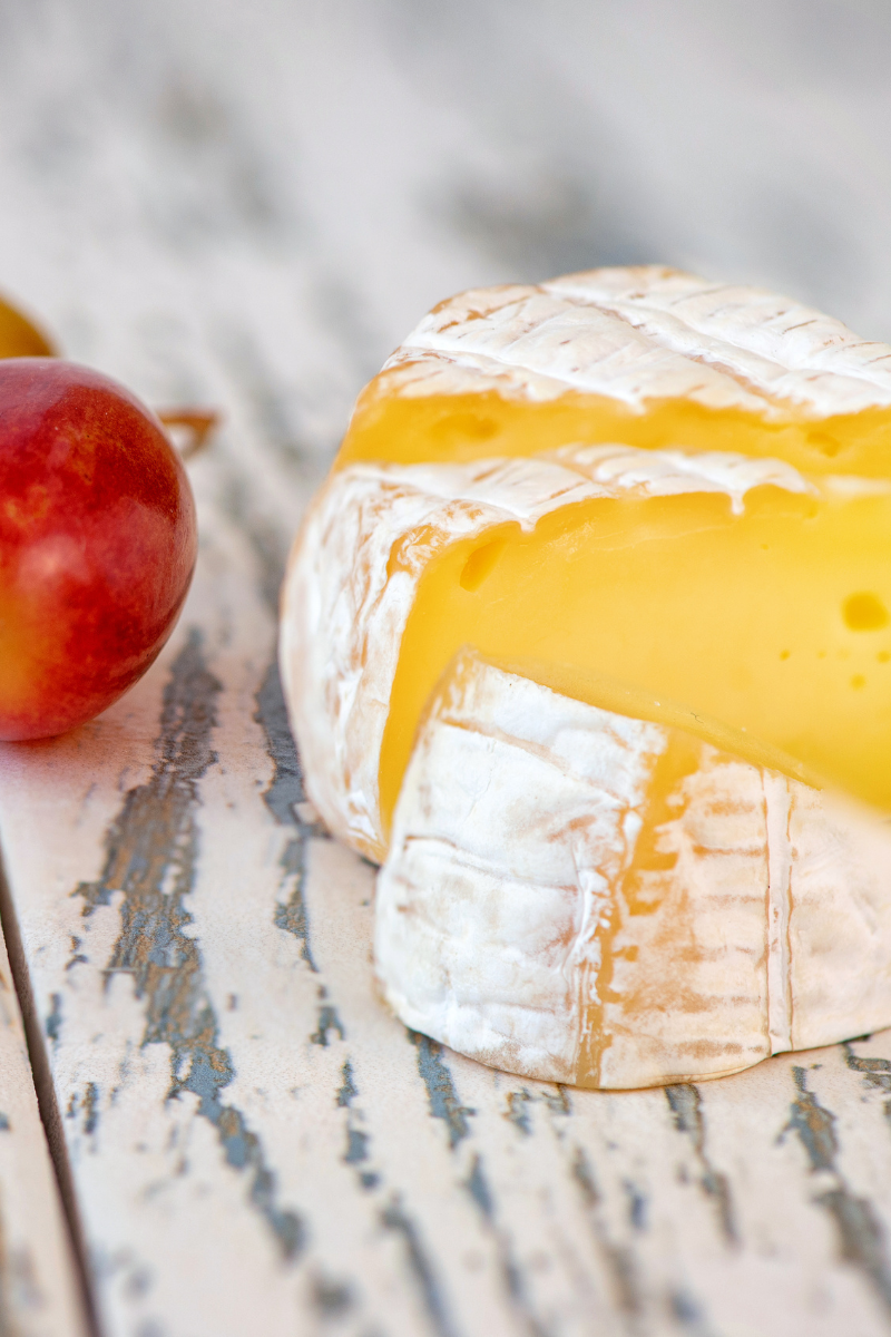 Soft ripened cheese (camembert) on a white wood surface.