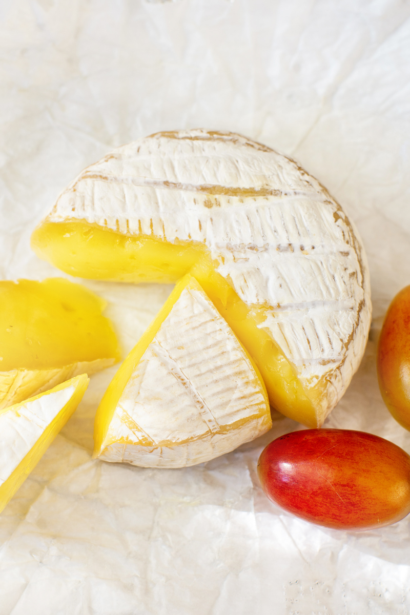 Soft ripened cheese (camembert) on a white wood surface.