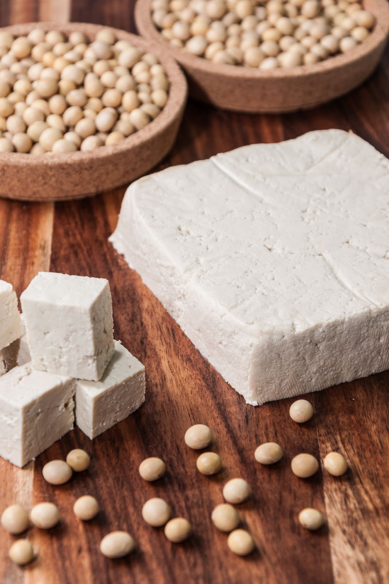cubes of tofu, and a block of tofu on a wooden surface, surrounded by whole soybeans.