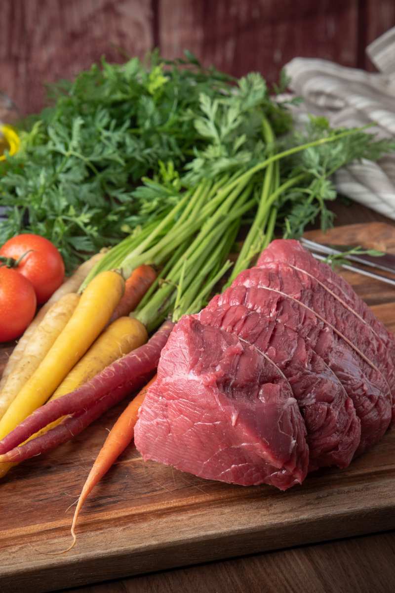 Top round beef cut on a wooden cutting board, surrounded by vegetables.